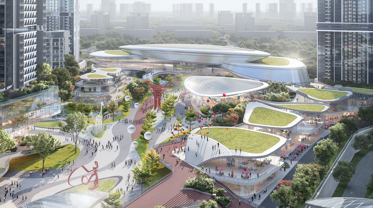 Aerial view of an open-air retail district with green-roofed pavilions, winding paths, sculptures and crowds of people