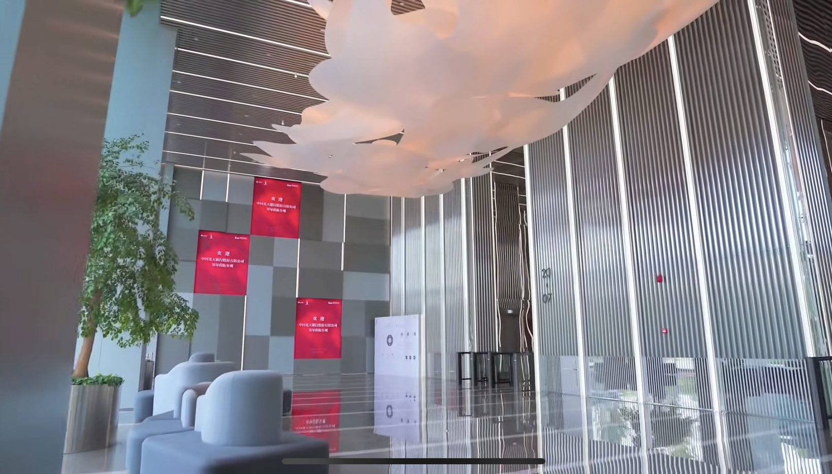 Photograph of the lobby with the cloud sculpture above seating and plants, red signage panels beyond