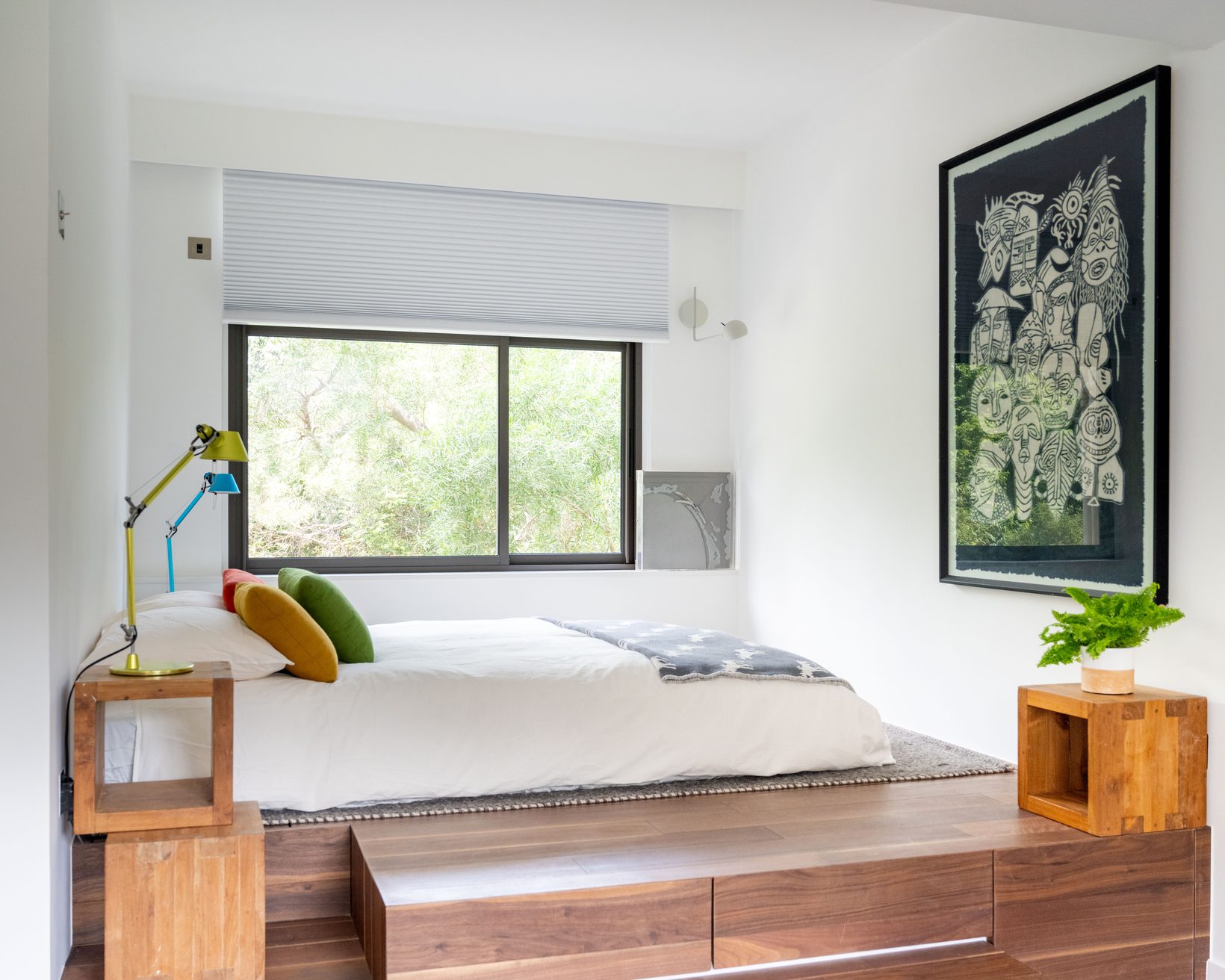 The bed on a raised timber platform by a window onto trees, a framed drawing on the wall