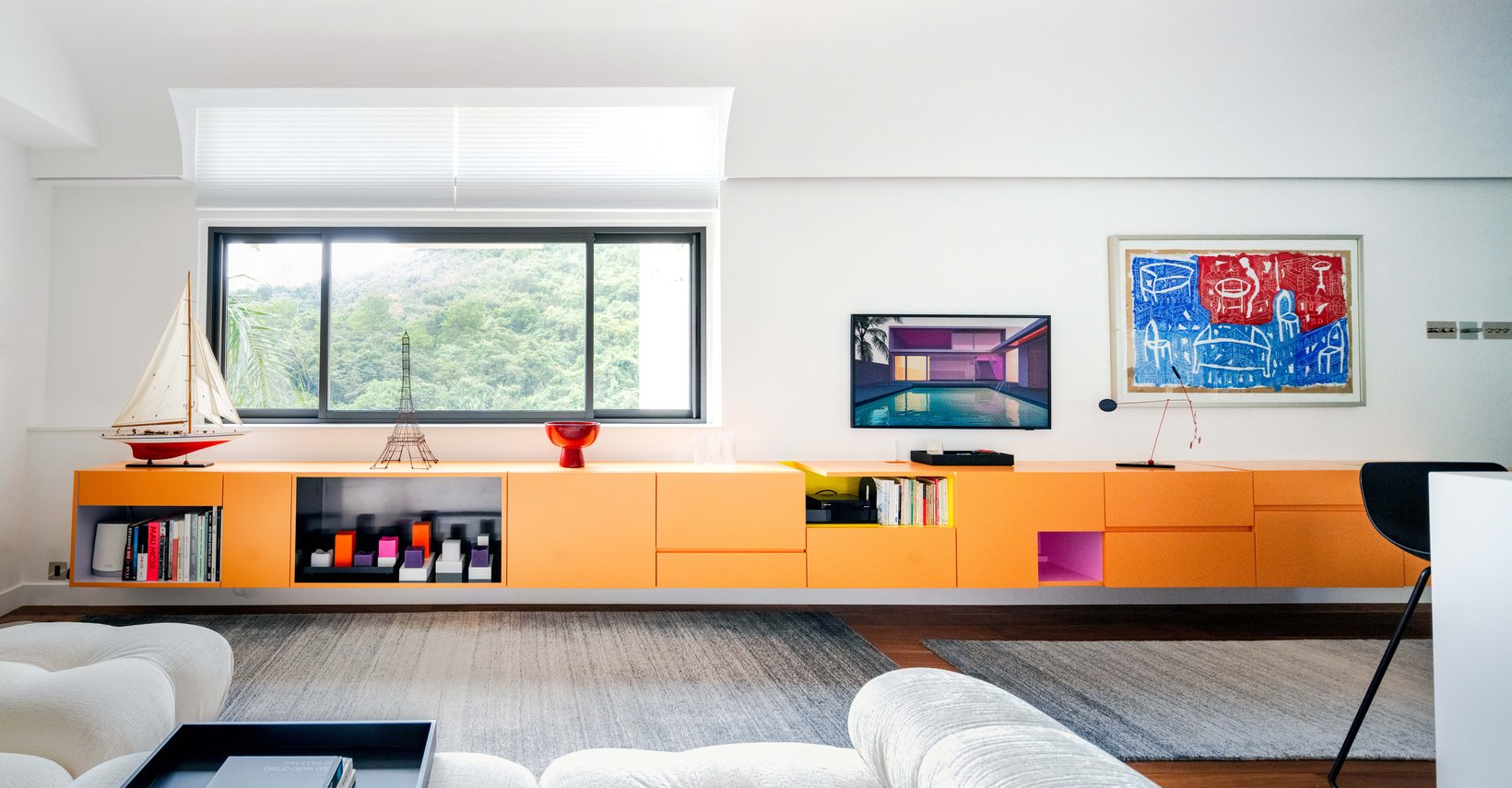 The living room: a long apricot cabinet floating beneath a window onto green hillside, with artwork and a white sofa