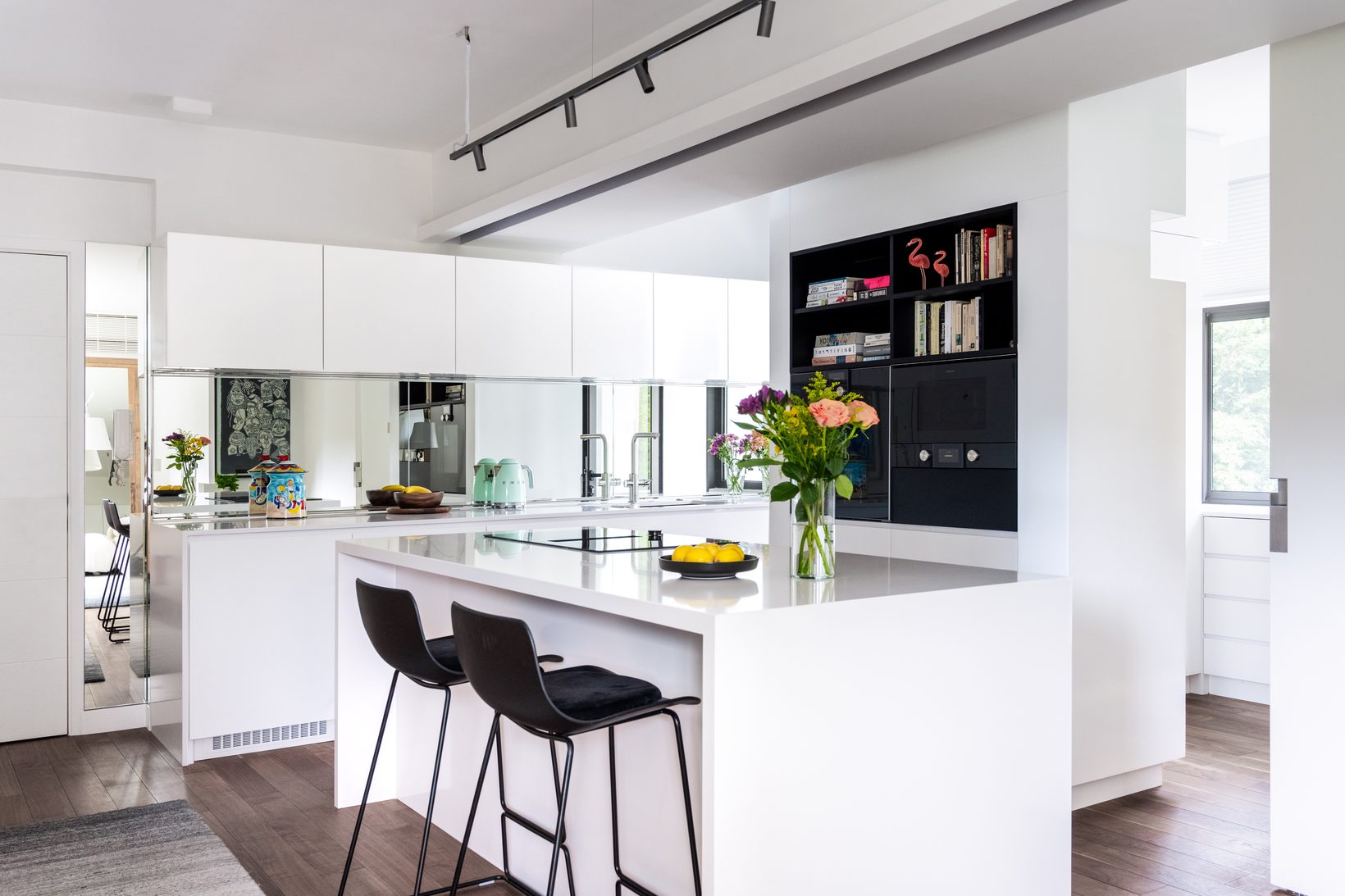 The kitchen island with stools, white cabinetry and a black shelving wall