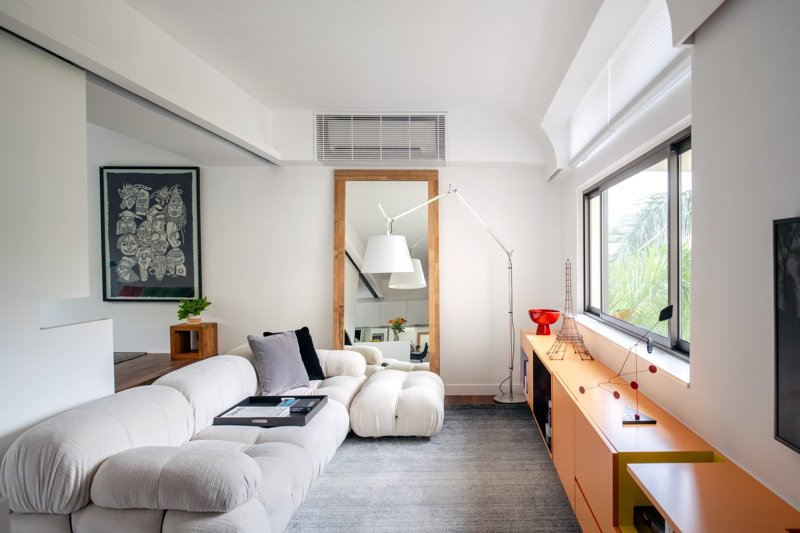 The living room from the sofa: a white sofa, a framed drawing, and a tall mirror reflecting the window