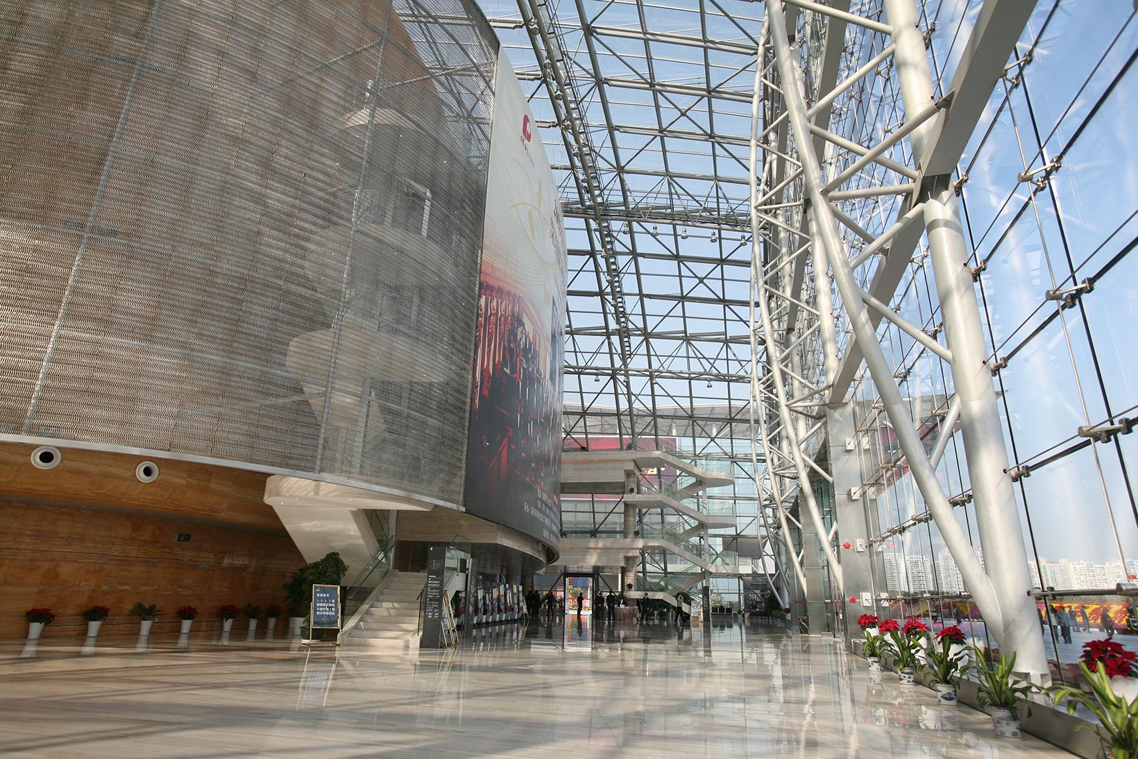 The foyer: the metal-clad oval on one side, a tall glass wall on white steel trusses on the other