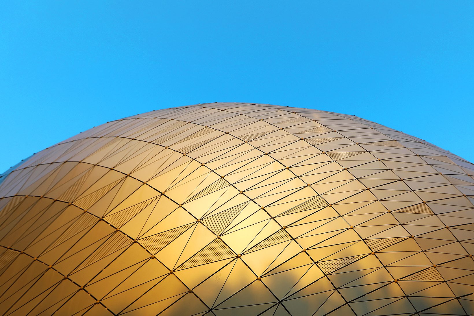 The top of the oval glowing gold against a deep blue sky
