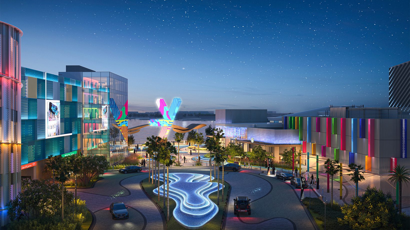 The arrival plaza at night, a lit water feature and the colourful SEVEN icon beyond