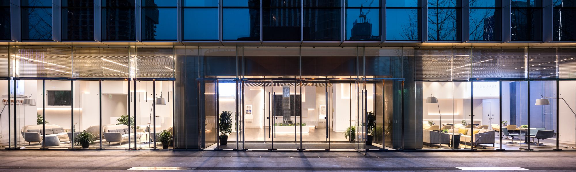Panoramic night view of the full glazed frontage, the interior glowing across the width of the building