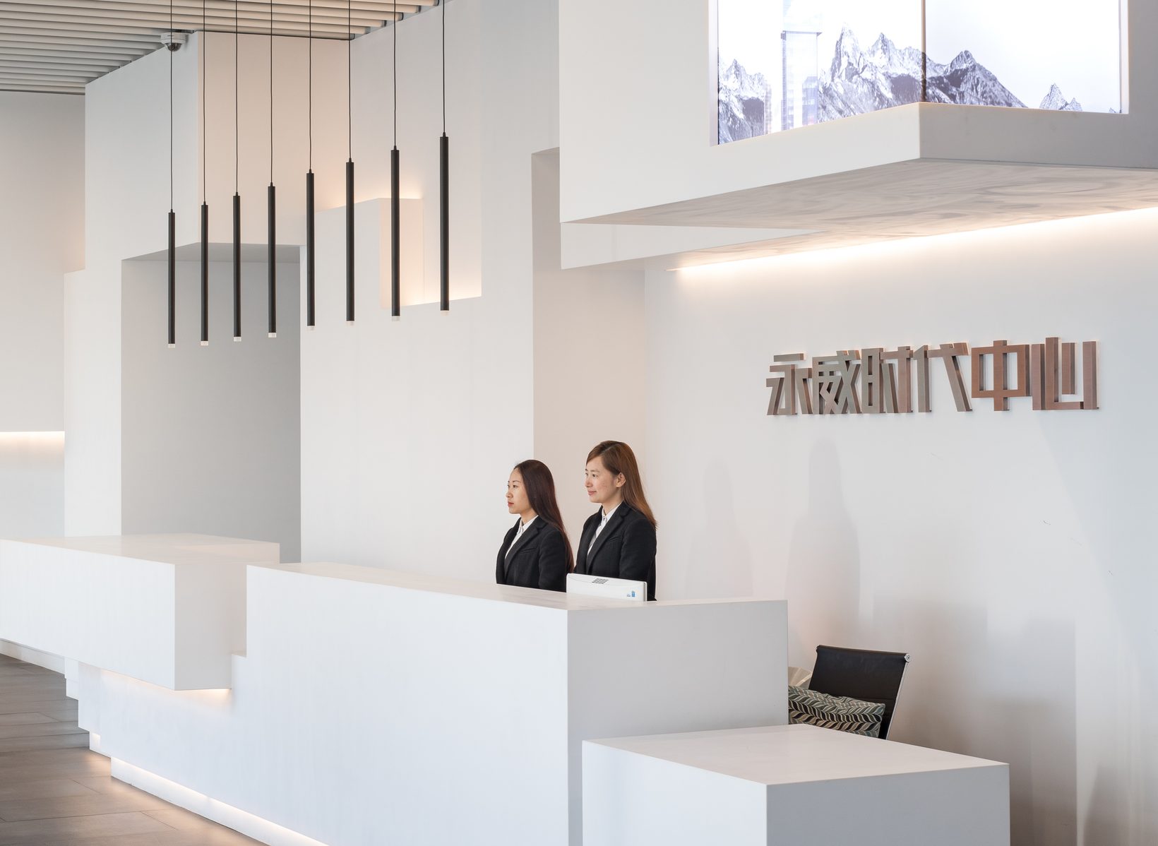 The reception desk stepping out of the white wall beneath pendant lights
