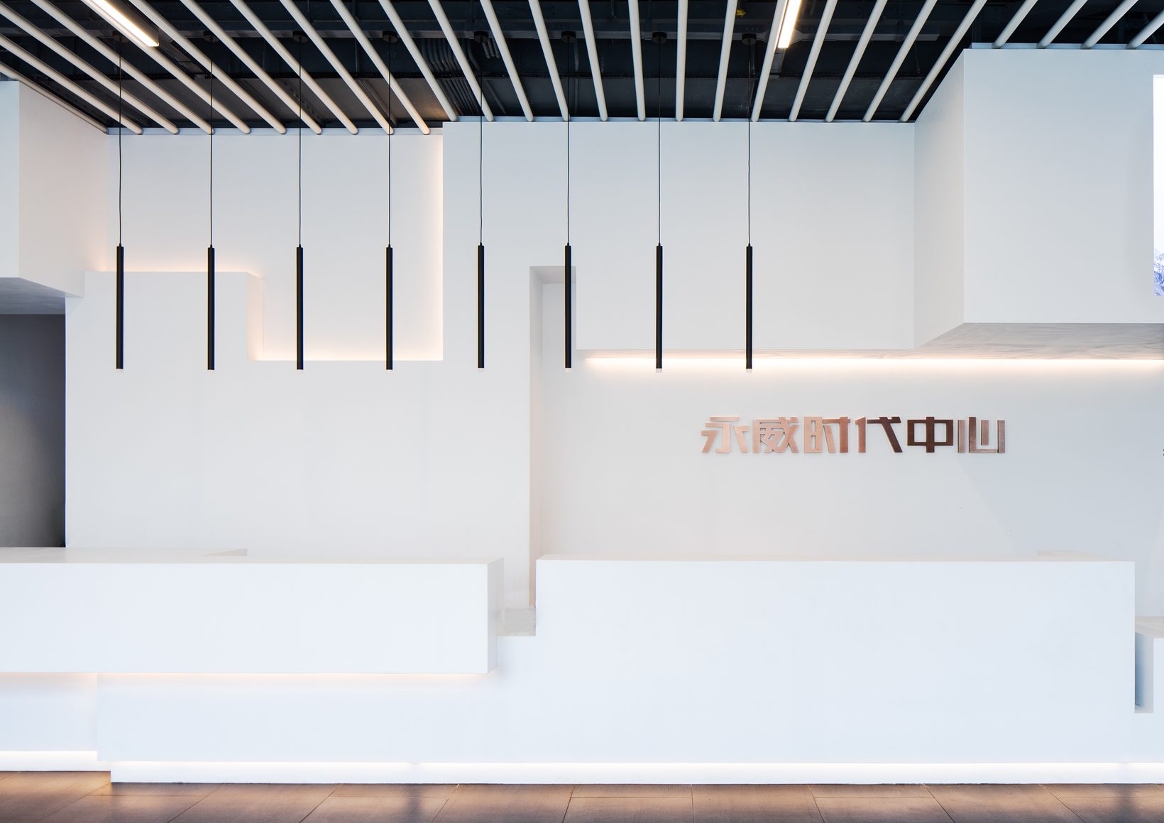 The feature wall above the reception, its white volumes stepping in and out, slim pendant lights hanging in front