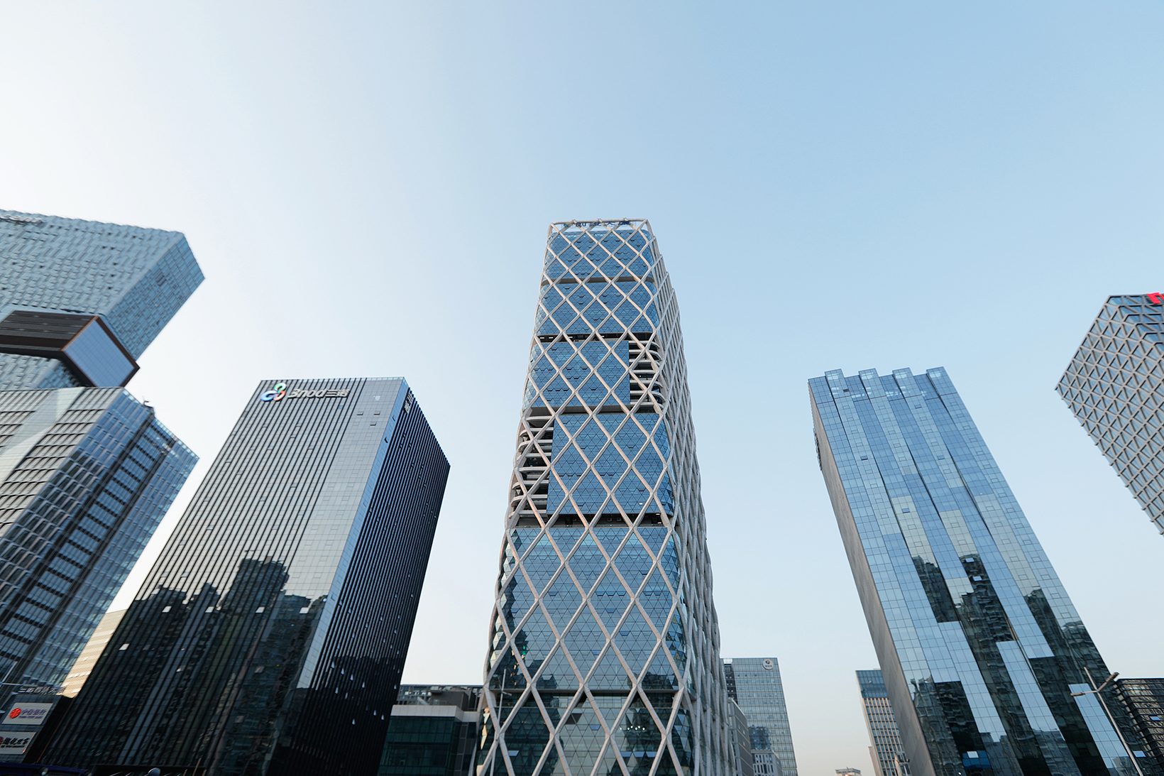 The tower seen from below among neighbouring towers, its diagrid bright against the sky