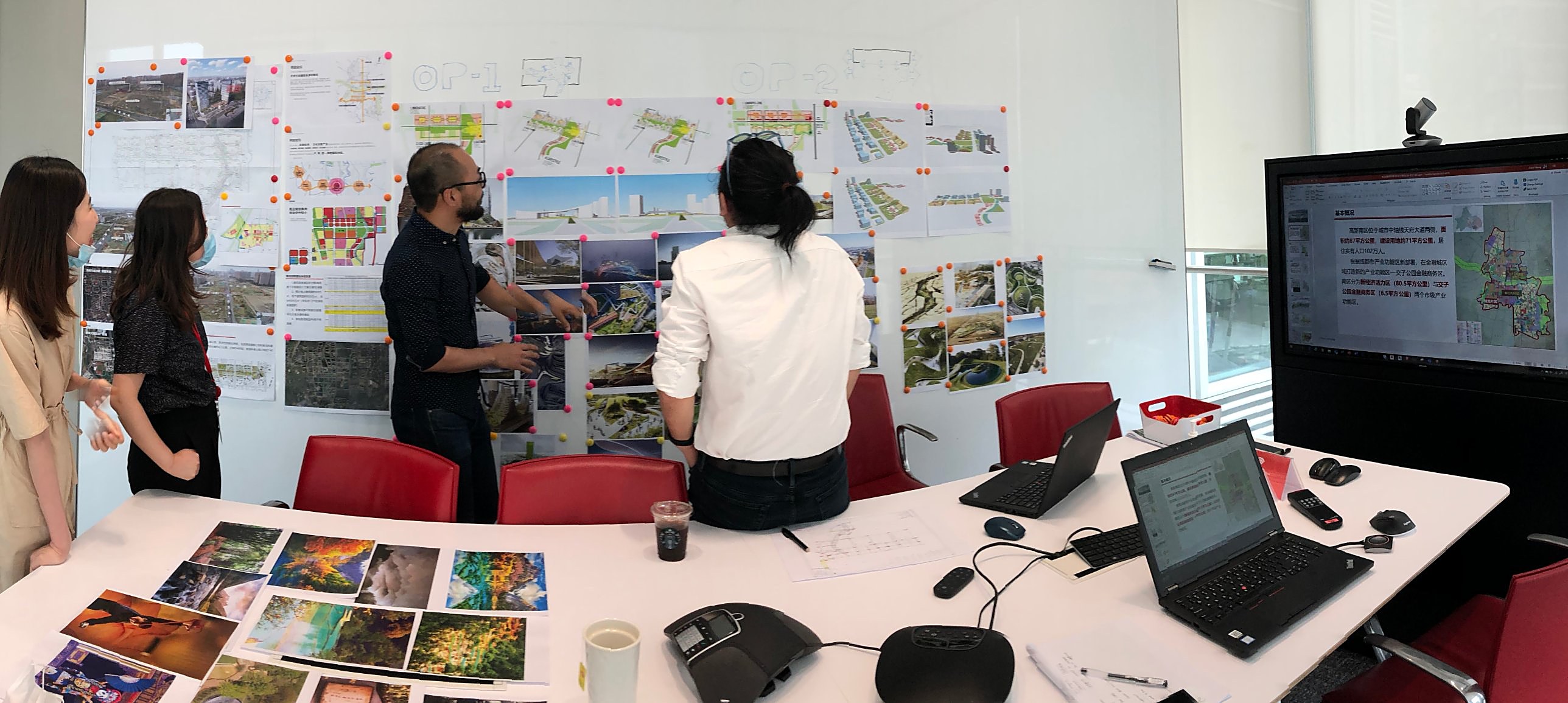 Design workshop: the team reviews masterplan options and reference images pinned to a wall, with study sheets spread across the table